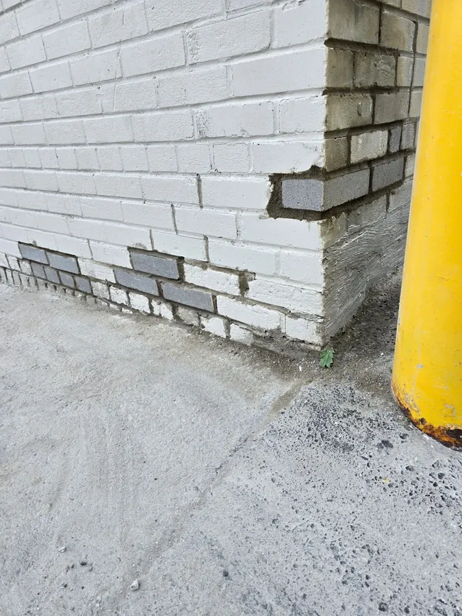 Painted brick wall base with grey replacement bricks set in fresh mortar beside an overhead door