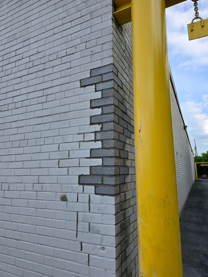 New grey bricks toothed into the corner of a painted brick wall with fresh mortar
