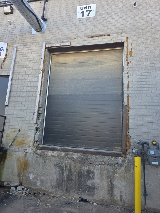 Rusted steel lintel and spalled masonry around a commercial overhead door opening awaiting replacement