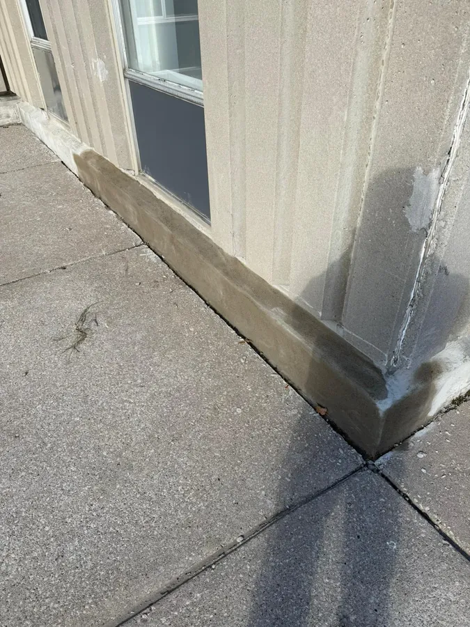 Freshly parged and caulked base of a precast concrete building wall along a sidewalk
