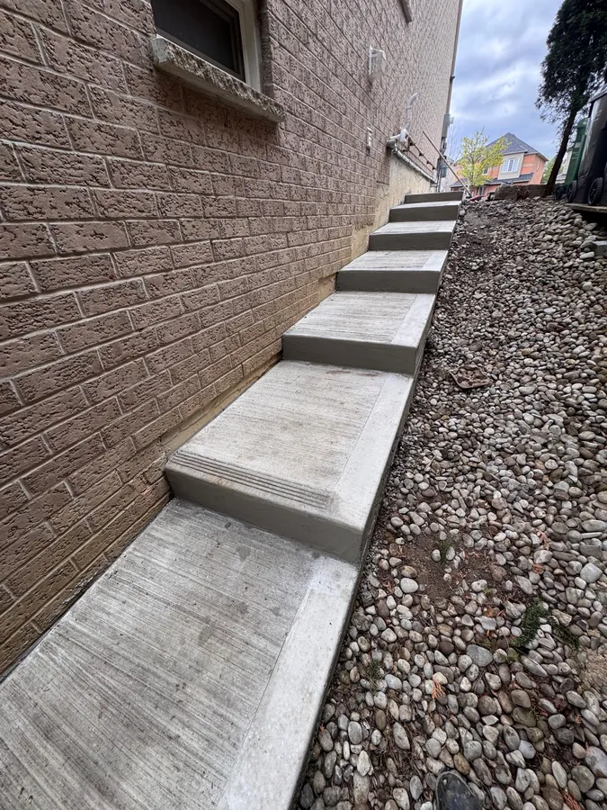 Completed stepped concrete walkway beside a building with tooled joints, broom finish and gravel drainage strip.