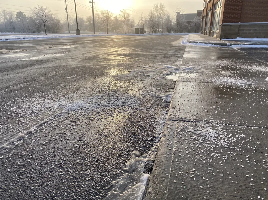 Granular ice-melt salt spread across a wet commercial parking surface and walkway