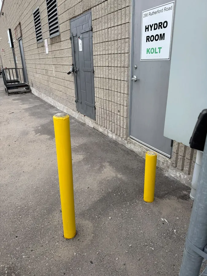 Two yellow steel bollards protecting a gas meter and regulator beside a loading dock door