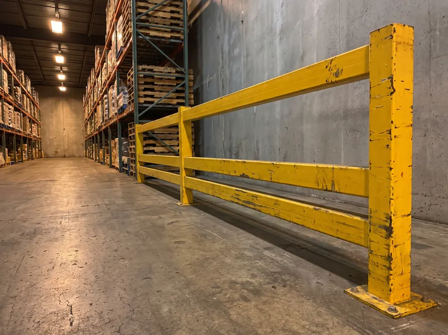 Yellow steel guard rail protecting pallet racking and wall from forklift impact