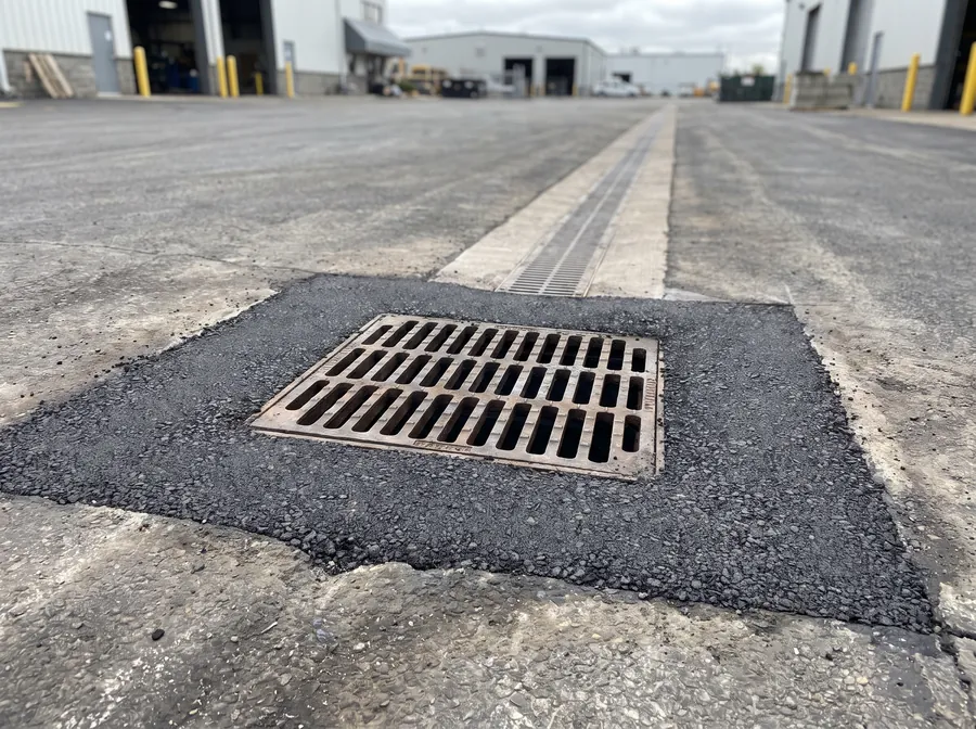 New cast-iron catch basin set flush in an asphalt yard with a trench drain beyond