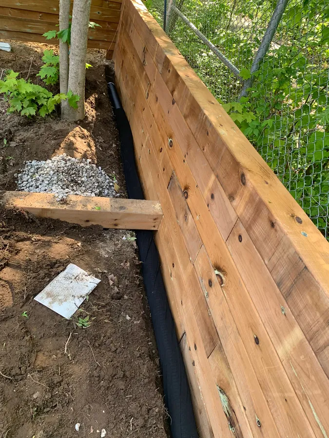 Clear drainage stone, geotextile filter fabric and a black drain pipe installed behind a new timber retaining wall