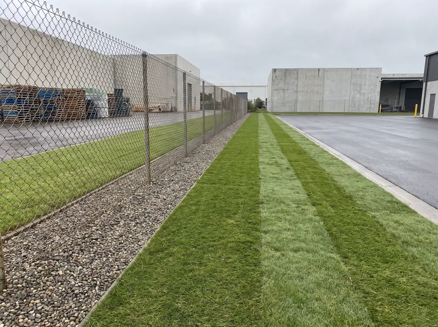 Tidy industrial fence line with vegetation cut back and a cleanly edged gravel strip