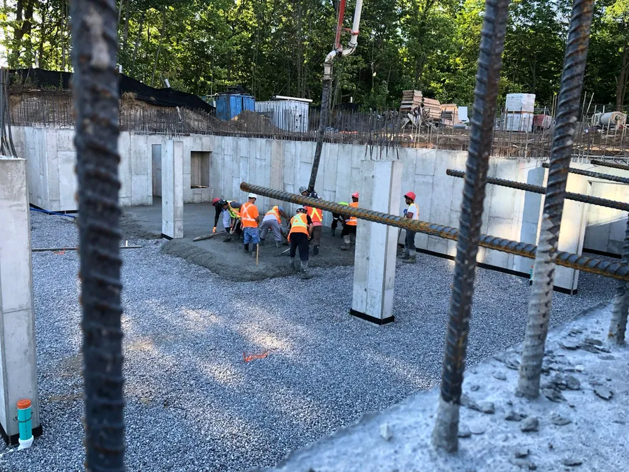 Crew placing concrete from a boom pump for a large slab inside cast-in-place foundation walls.