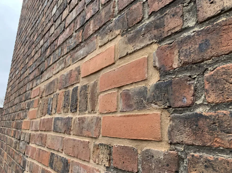 Repointed industrial brick wall with fresh mortar joints meeting older weathered work