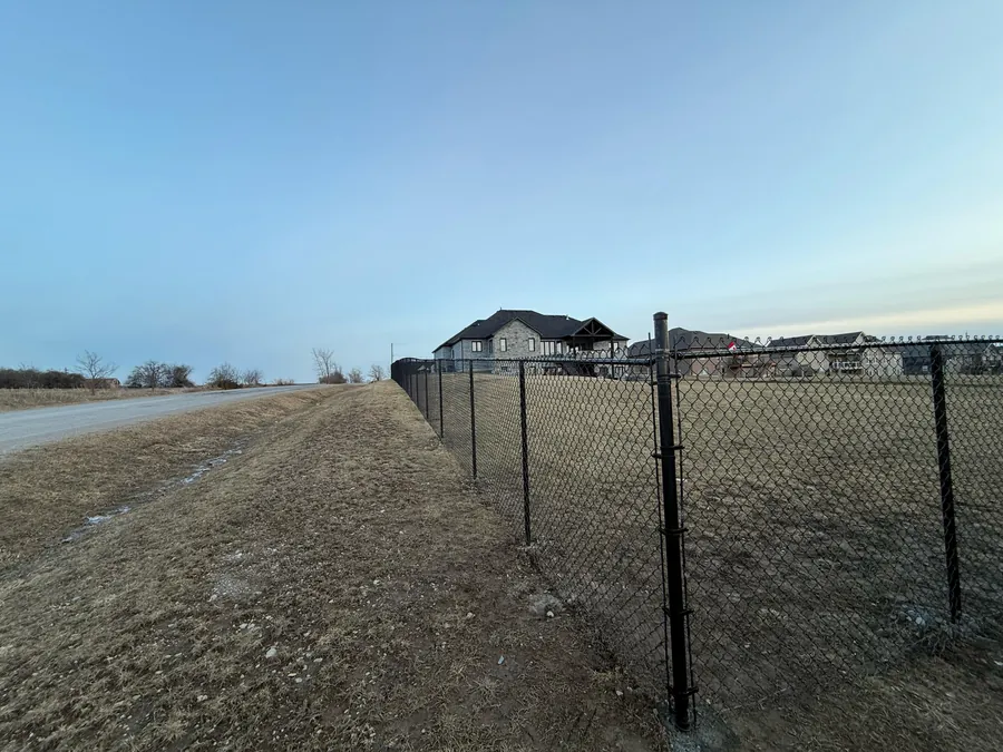 Long black PVC-coated chain-link perimeter fence with top rail running along a property boundary at dusk