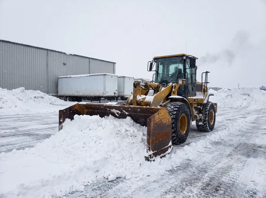 Wheel loader with a snow pusher box clearing a large industrial yard