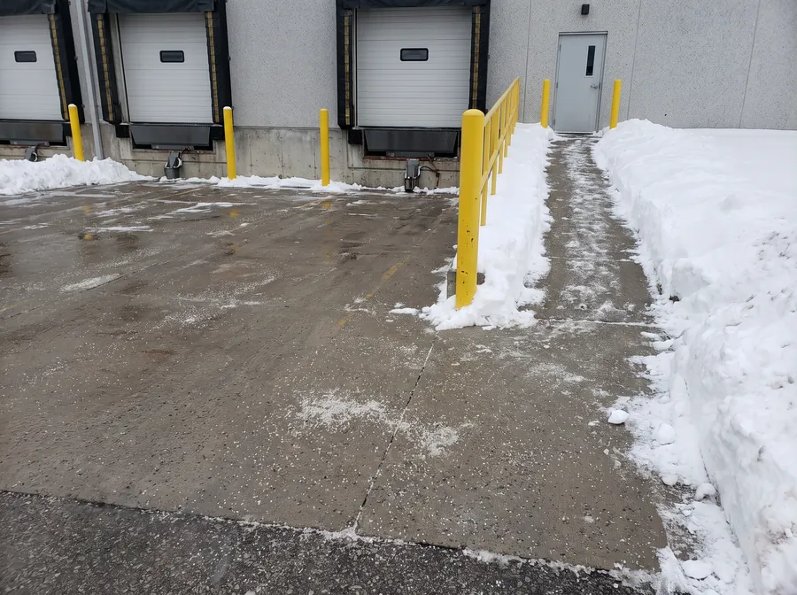 Cleared and salted loading dock apron with yellow protective bollards and walkway