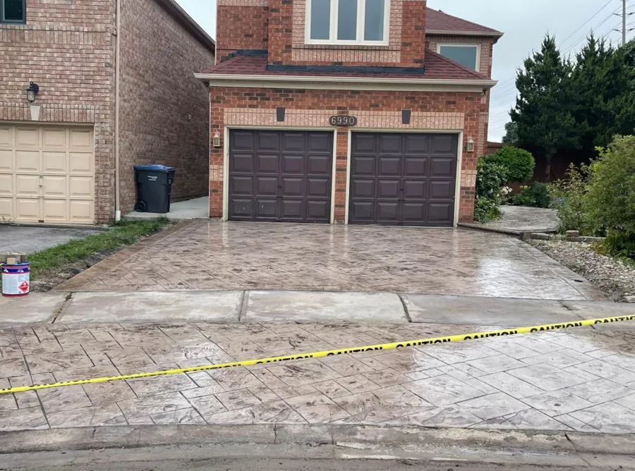 Stamped concrete driveway in an ashlar slate pattern, wet and glossy, running up to a two-car garage.