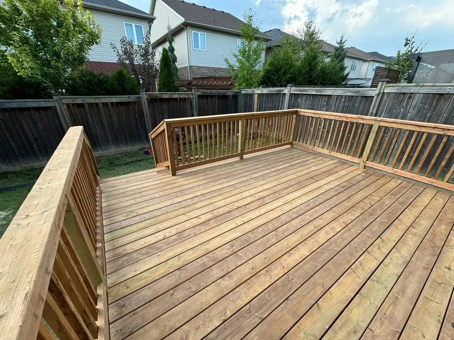 Newly built pressure-treated pine deck with a matching square-baluster wood railing and solid privacy wall in a fenced backyard.