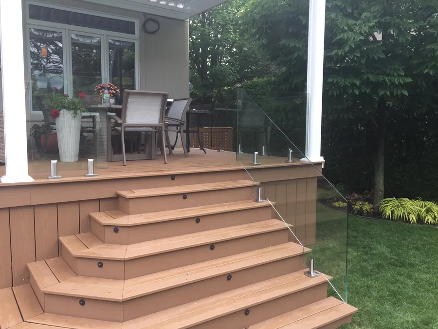 Frameless glass railing on polished stainless spigots edging a raised deck, carried down wide cascading stairs with black riser lights.