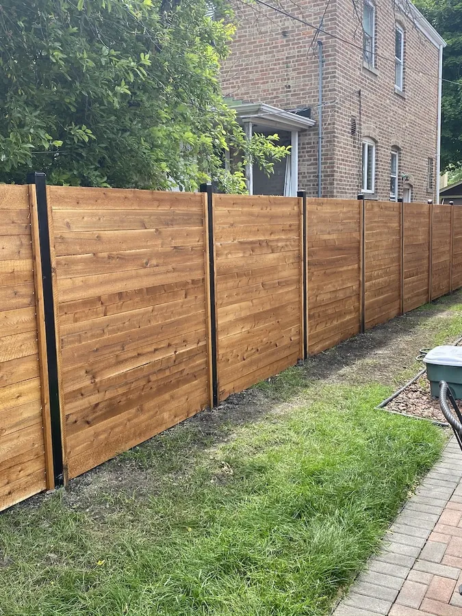 Horizontal cedar board privacy fence with black steel posts running along a residential backyard lawn
