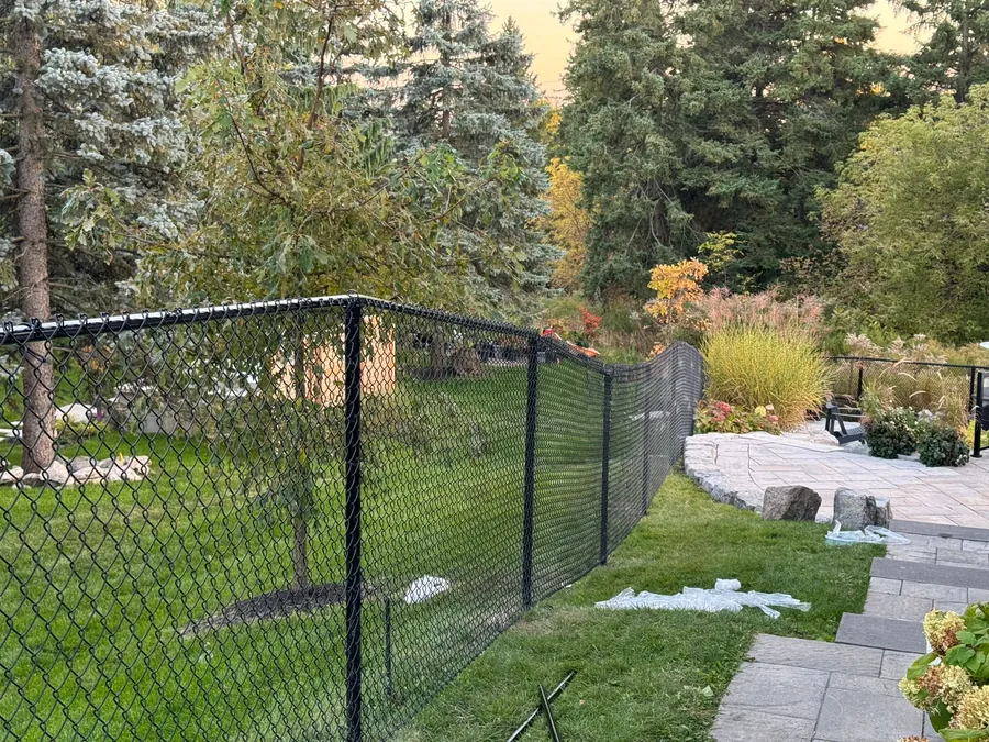 Black chain-link fence with privacy mesh bordering a landscaped backyard and flagstone patio at dusk