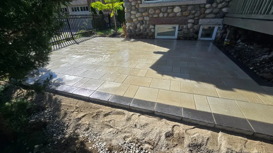 Sunlit patio of large-format cream concrete pavers with a charcoal soldier-course border