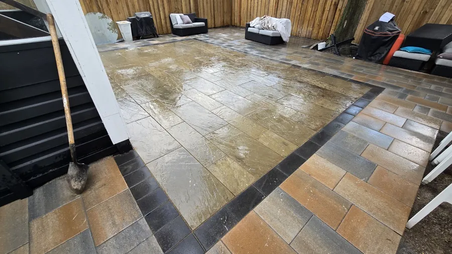 Rain-wet natural cleft flagstone patio field framed by charcoal and tan paver borders