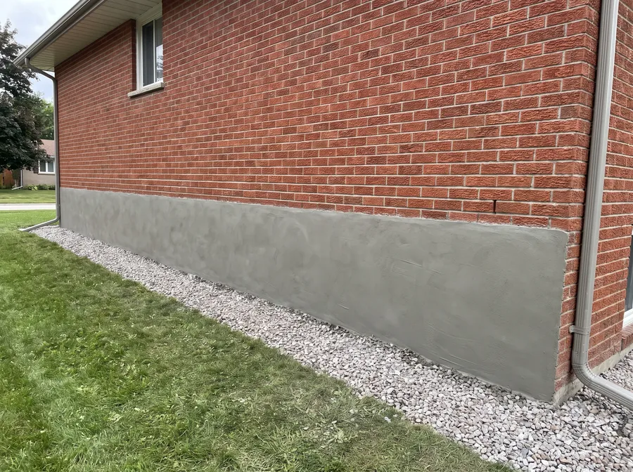 Smooth grey parge coating applied over an exposed block foundation to a clean line