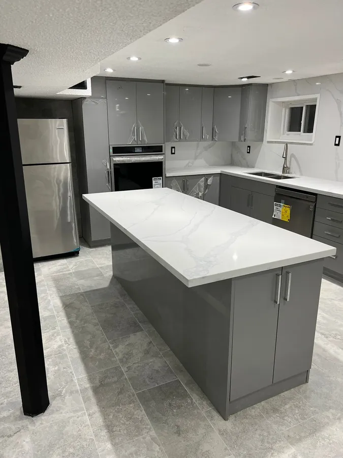 Finished kitchen with gloss grey cabinets, white quartz island, marble-look backsplash and large tile flooring.