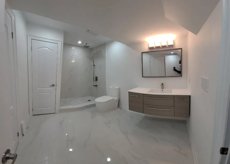 Renovated bathroom with floating wood vanity, framed mirror, marble-tiled walk-in shower and polished porcelain floor.